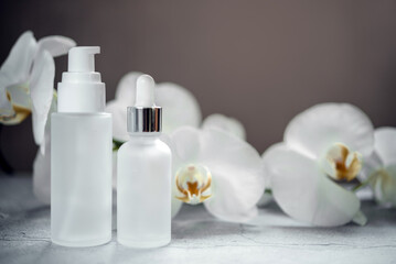 Fototapeta na wymiar White glass serum bottle, lotion pump bottle and cream jar mock-ups in the bathroom with orchid flowers in the background, unbranded cosmetic products, spa cosmetic product branding mockup