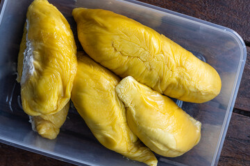 Close-up overhead view of golden yellow musang king durian pulp flesh in container on wooden surface