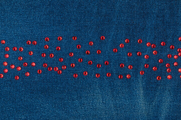 Red rhinestones lying in a line on worn denim. With space for design, text place.
