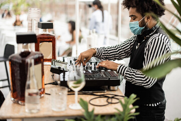 African dj playing music at cocktail bar outdoor while wearing face safety mask - Main focus on top...