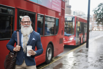 Senior business man going to work drinking coffee with london bus station in background - Focus on...