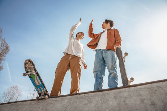 Two boys skaters stand on the highest ramp in a skatepark and encourage each other for a great workout, holding skateboards in their hands