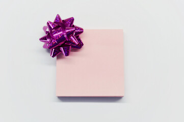 Pink shiny bow for gift and paper for notes on white background