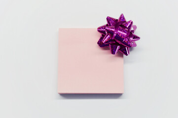 Pink shiny bow for gift and paper for notes on white background