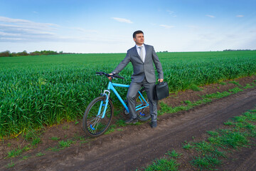 Obraz premium Businessman with a bicycle posing in a green grass field - business concept for freedom, vacation or freelance. Beautiful spring nature.