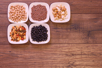 Frutos secos y legumbres en plato pequeño blanco sobre fondo de madera.