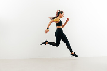 Fototapeta na wymiar Runner in sport clothes sprinting near a white wall. Woman with kinesiology tape on shoulder jogging indoors.