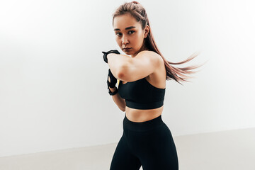 Woman doing kickboxing workout against a white wall. Female practicing punches.
