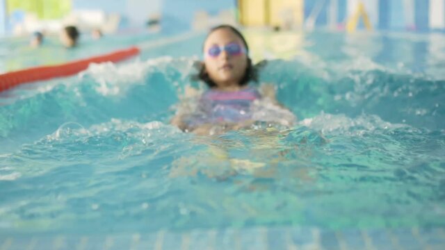 Happy child in swimming pool. Sports lifestyle concept. Girl at swimming lessons. The girl pushes off the side and swims away into the distance, the focus remains in the foreground.