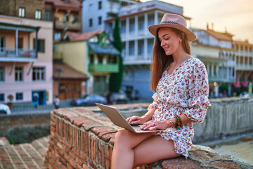 Happy cheerful smiling beautiful cute joyful young girl using laptop outdoors in Tbilisi city