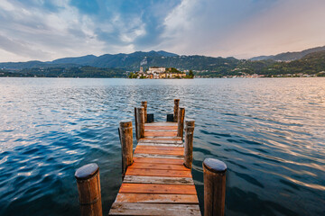 Obraz premium Orta San Giulio / Italy - June 2021: The island of San Giulio with a wooden jetty in the foreground at sunset