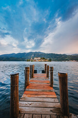 Orta San Giulio / Italy - June 2021: The island of San Giulio with a wooden jetty in the foreground at sunset