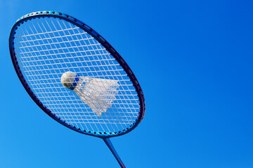 Badminton racket with shuttlecock against blue sky. Badminton open air game activity. Badminton outdoor sport playing. Close up view with copy space.