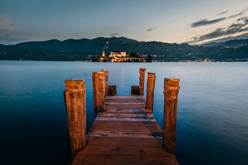 Orta San Giulio / Italy - June 2021: The island of San Giulio with a wooden pier in the foreground at sunset (blue hour), long exposure