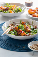 Close up of a grilled peach and arugula salad garnished with sunflower seeds, lit from the back.
