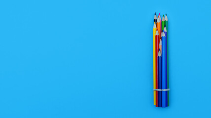 Colored wooden pencils on a blue paper background. Vertically upwards, place for text about school or drawing lessons.
