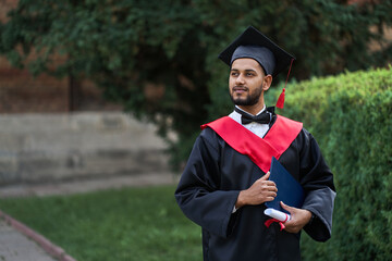 Indian graduate in graduation robe with diploma in university campus copy space