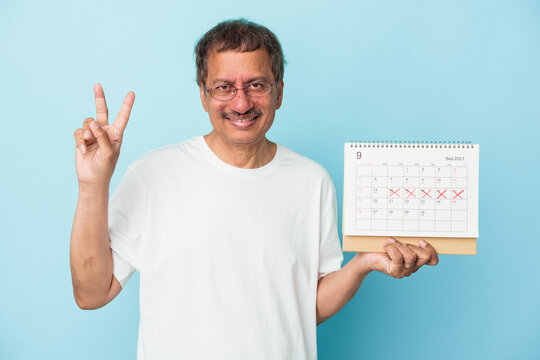Senior indian man holding a calendar isolated on blue background showing number two with fingers.