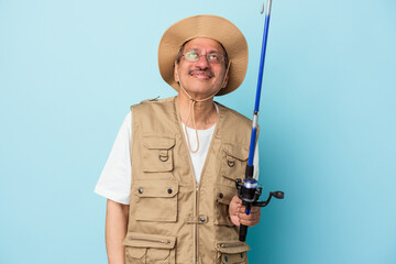 Senior indian fisherman holding rod isolated on blue background dreaming of achieving goals and purposes