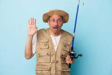 Senior indian fisherman holding rod isolated on blue background surprised and shocked.