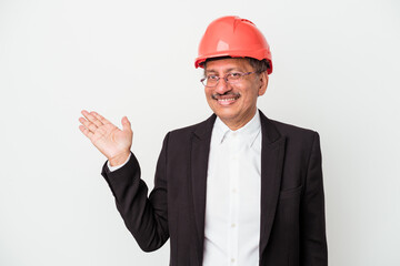 Middle aged indian architect man isolated on white background showing a copy space on a palm and holding another hand on waist.