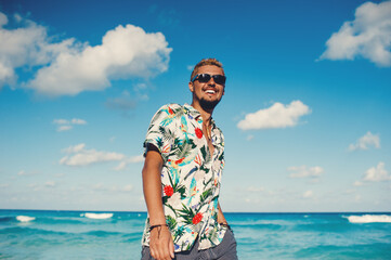 Young tourist man wearing hawaiian shirt at the sea or the ocean background. Travel vacation holiday. Man walking at the sea, enjoy tropical season - obrazy, fototapety, plakaty