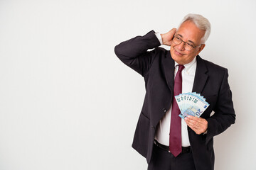 Senior american business man holding bills isolated on white background touching back of head, thinking and making a choice.