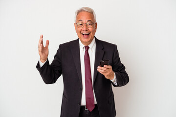 Senior business american man holding mobile phone isolated on white background receiving a pleasant surprise, excited and raising hands.