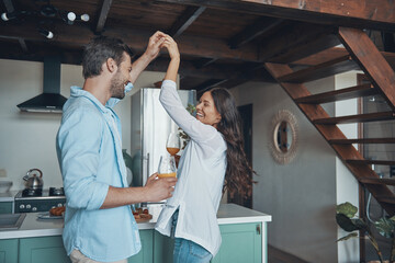 Beautiful young couple smiling and dancing while spending time in the kitchen