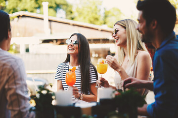 Group of young people laughing and drinking cocktails at a summer bar during the day