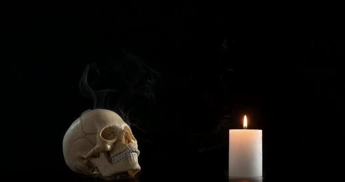 Magical ceremony in the dark. A view of a magic caremony with a human skull and burning candle against black background.