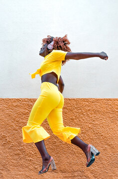 Chica afro africana, con vestido amarillo y cascos de m&uacute;sica, saltando de alegr&iacute;a.