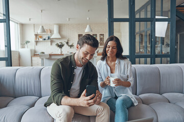 Beautiful young couple drinking coffee and communicating while sitting on the sofa at home