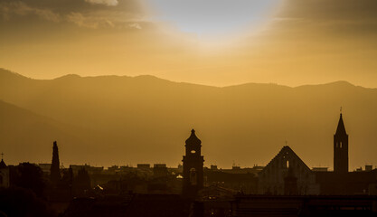 Obraz premium The rooftops and church towers of Pisa, Italy, silhouetted by a beautiful sunrise, with the mountains in the background