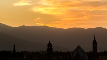 The rooftops and church towers of Pisa, Italy, silhouetted by a beautiful sunrise, with the mountains in the background
