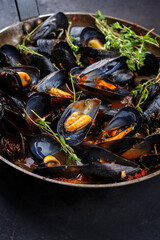 Traditional barbecue Italian blue mussel in tomato red wine sauce with herb and garlic as close-up in a rustic iron pan