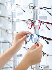 Woman choosing the glasses in optics store, eyesight and vision concept.