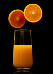 Orange juice in a glass with fruit slice hovering on the dark black background