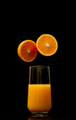 Orange juice in a glass with fruit slice hovering on the dark black background