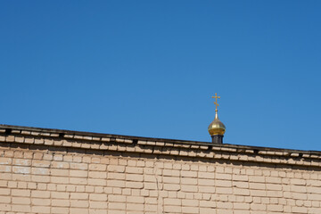 The dome of the church behind the brick wall against the clear blue sky.