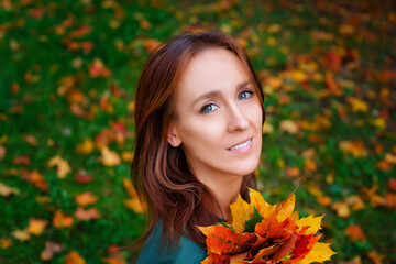Naklejka na ściany i meble A beautiful young woman with a bouquet of yellow-red maple leaves in the park against the background of fallen foliage.