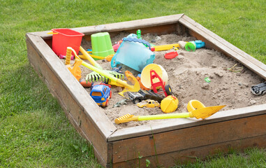 children's sandbox with toys on green grass - obrazy, fototapety, plakaty