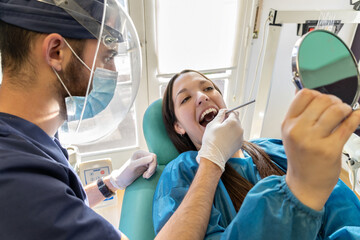 Young dentist in mask examining teeth of female client