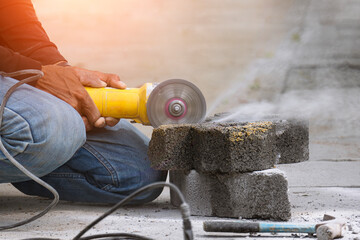 Close up of worker hand using grinder cutting turf stone block for paving sidewalk in public area