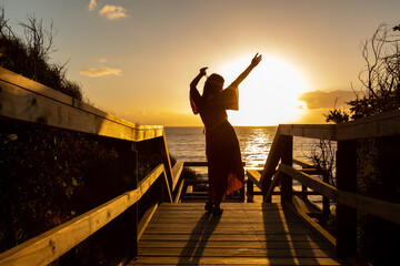 silhouette of young woman with arms in the air celebrate life against sunset at the beach