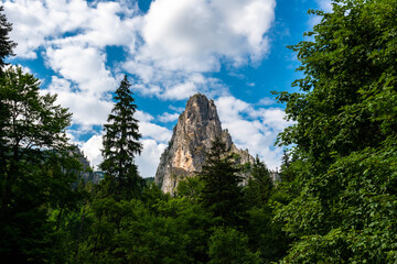 Beautiful mountain with a catholic cross surrounded by green forest, blue sky with white clouds in Romania.