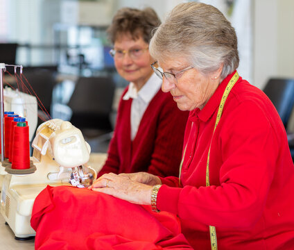 older lady sewing with red fabric while another looks on