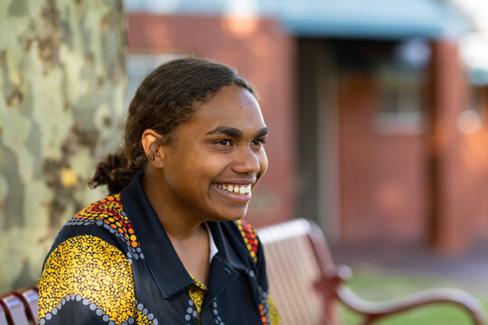 happy teenaged aboriginal girl sitting on bench in shade