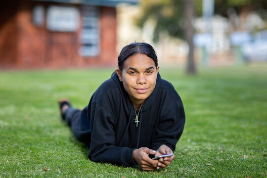 teenager lying on grass with mobile phone in hands