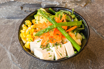 Vegan poke bowl with wild asparagus, carrot, pieces of tofu, crushed chives, sweet corn, avocado,...